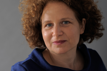 Gaby Hönig. Frau mit lockigen braunen mittellangen Haaren. Sie trägt Lippenstift und einen blauen Pullover. Zuständig für Coaching, Fortbildungen, Konfliktmanagement, Moderation & Supervision.