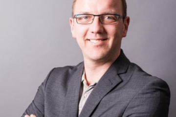Jan Ulrich-Hey. Lächelnder Mann mit eckiger Brille, grauem Sakko und kurzen Haaren. Zuständig für Coaching, Konfliktmanagement, Organisationsentwicklung & Supervision.