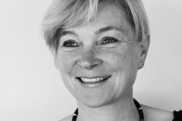Katrin Brandner. Lächelnde Frau mit kurzen hellen Haaren und einer dunklen Perlenkette & Top. Zuständig für Coaching, Konfliktmanagement, Moderation, Organisationsentwicklung & Supervision.